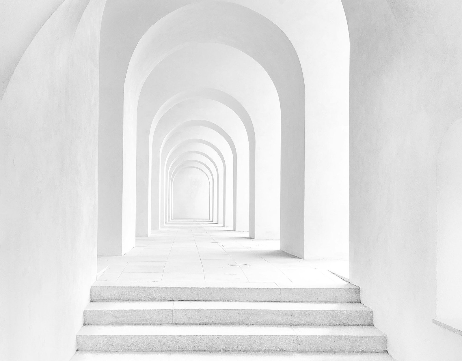 A bright sequence of white arches receding toward a softly lit passage.